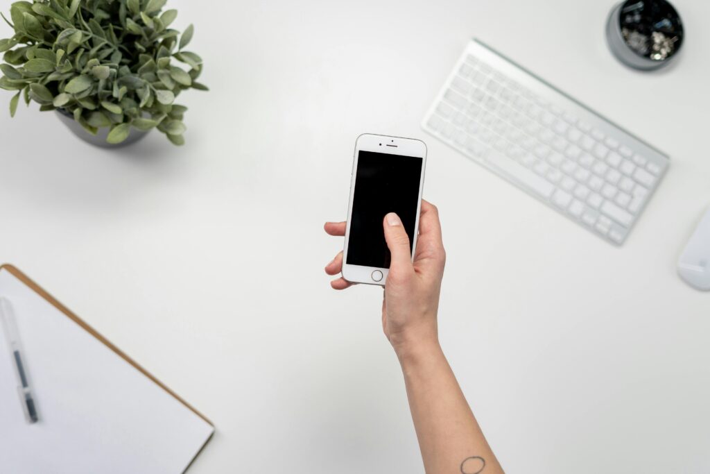 Top view of a minimalist workspace featuring a smartphone, keyboard, and plant.