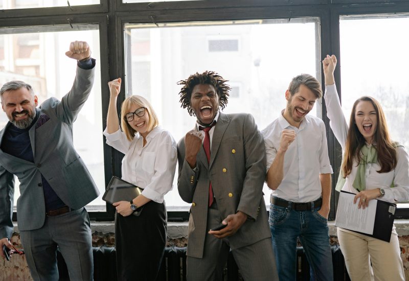 A joyful, diverse group of colleagues celebrating success indoors with cheerful expressions.