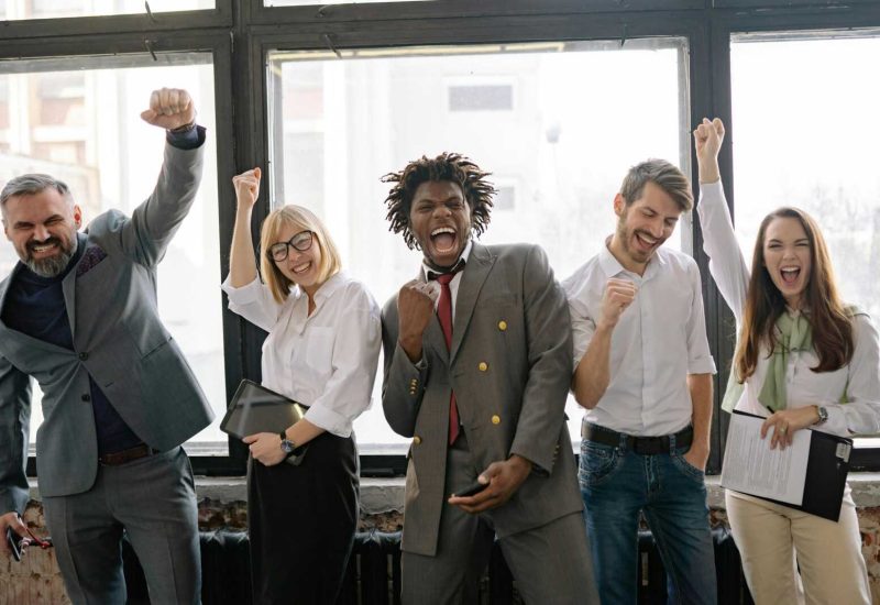 A joyful, diverse group of colleagues celebrating success indoors with cheerful expressions.